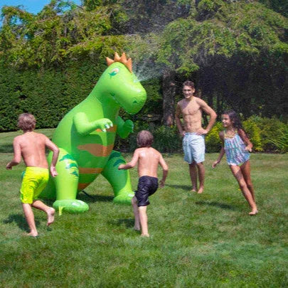 Enfants jouant autour d’un arroseur dinosaure gonflable sur une pelouse en été