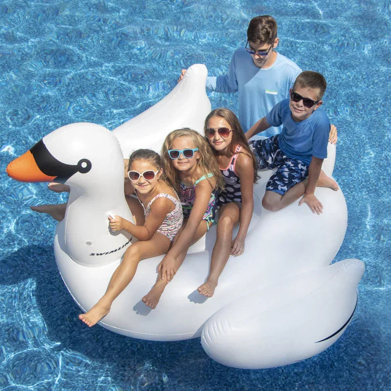 Enfants profitant d'une piscine sur une bouée cygne géante, ambiance estivale familiale.