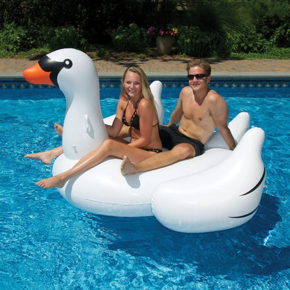 Deux personnes sur un grand matelas gonflable cygne blanc dans une piscine bleue