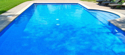 Piscine extérieure avec liner bleu effet galets, terrasse en béton et chaises longues
