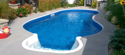Piscine creusée bleue moderne entourée de végétation et terrasse en béton, idéale jardin.