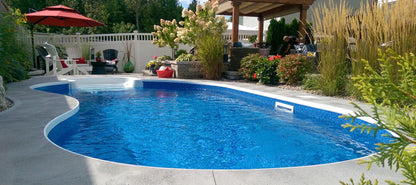 Piscine creusée moderne entourée de végétation, terrasse et mobilier extérieur
