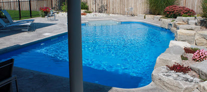 Piscine creusée extérieure avec margelle en pierre, eau bleue, terrasse et aménagement paysager