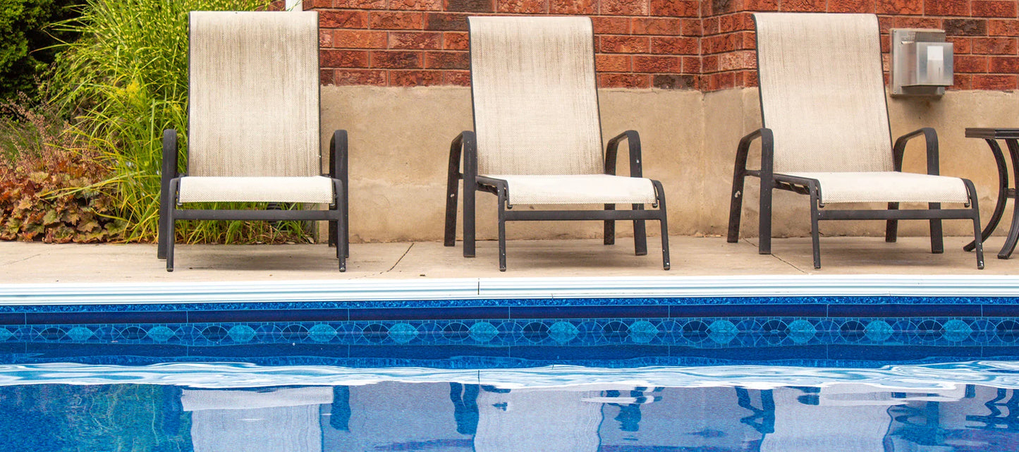 Bord de piscine creusée avec carrelage bleu et trois chaises longues sur terrasse
