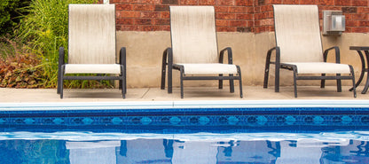 Bord de piscine creusée avec carrelage bleu et trois chaises longues sur terrasse