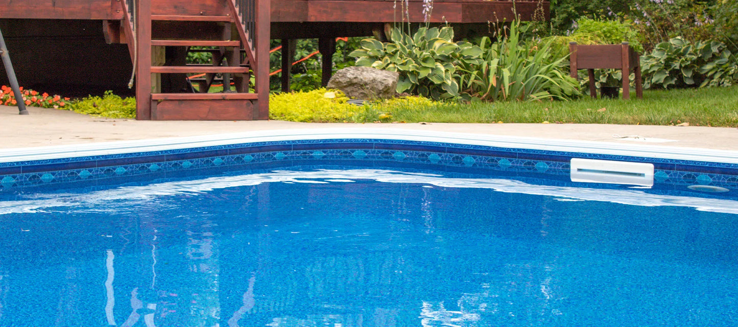 Piscine creusée extérieure avec liner bleu, margelle et jardin paysager en arrière-plan