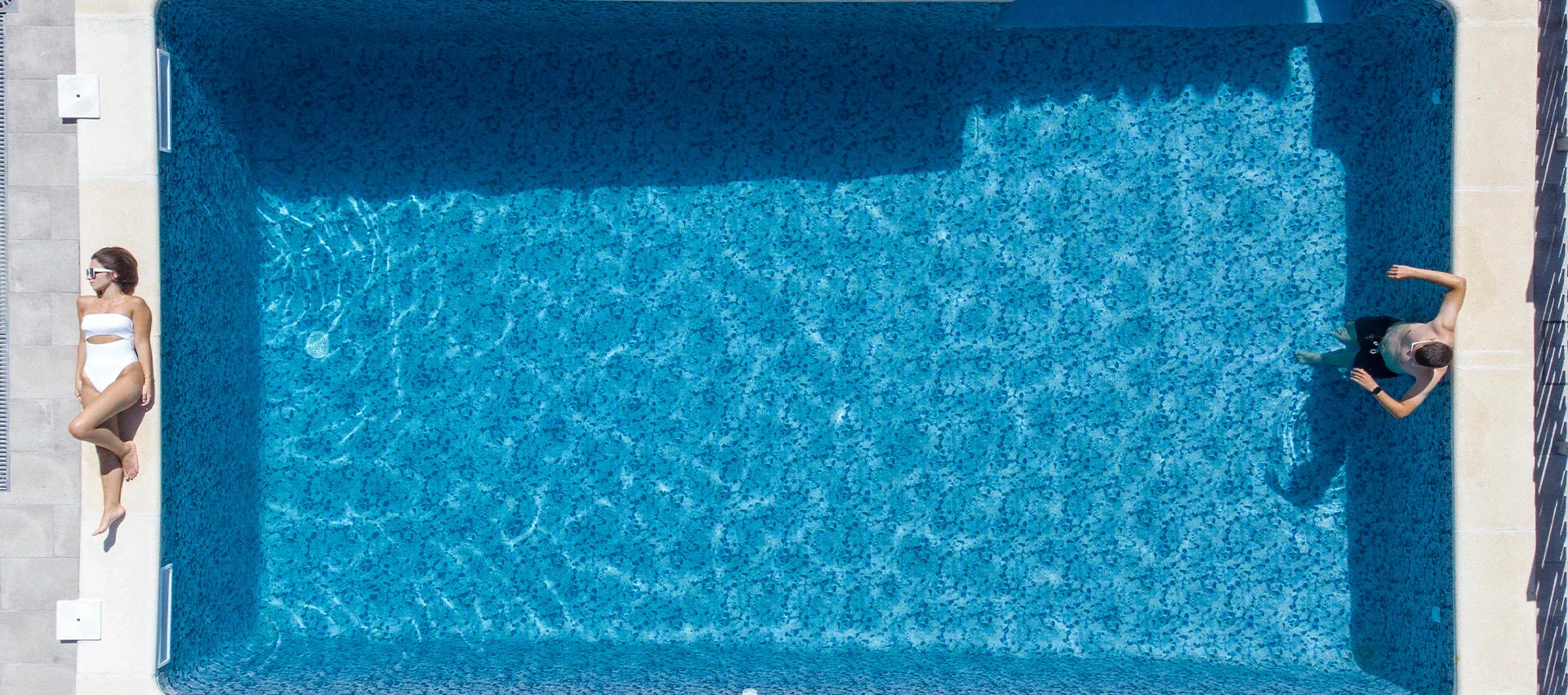 Vue aérienne d'une piscine moderne avec une femme au bord et un homme dans l'eau bleue