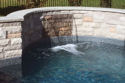 Cascade d'eau moderne sur mur en pierre dans une piscine extérieure, carrelage mosaïque gris.