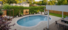 Piscine creusée moderne dans un jardin paysager avec terrasse, mobilier et végétation luxuriante