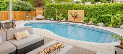Piscine creusée moderne entourée de terrasse, mobilier extérieur et aménagement paysager.