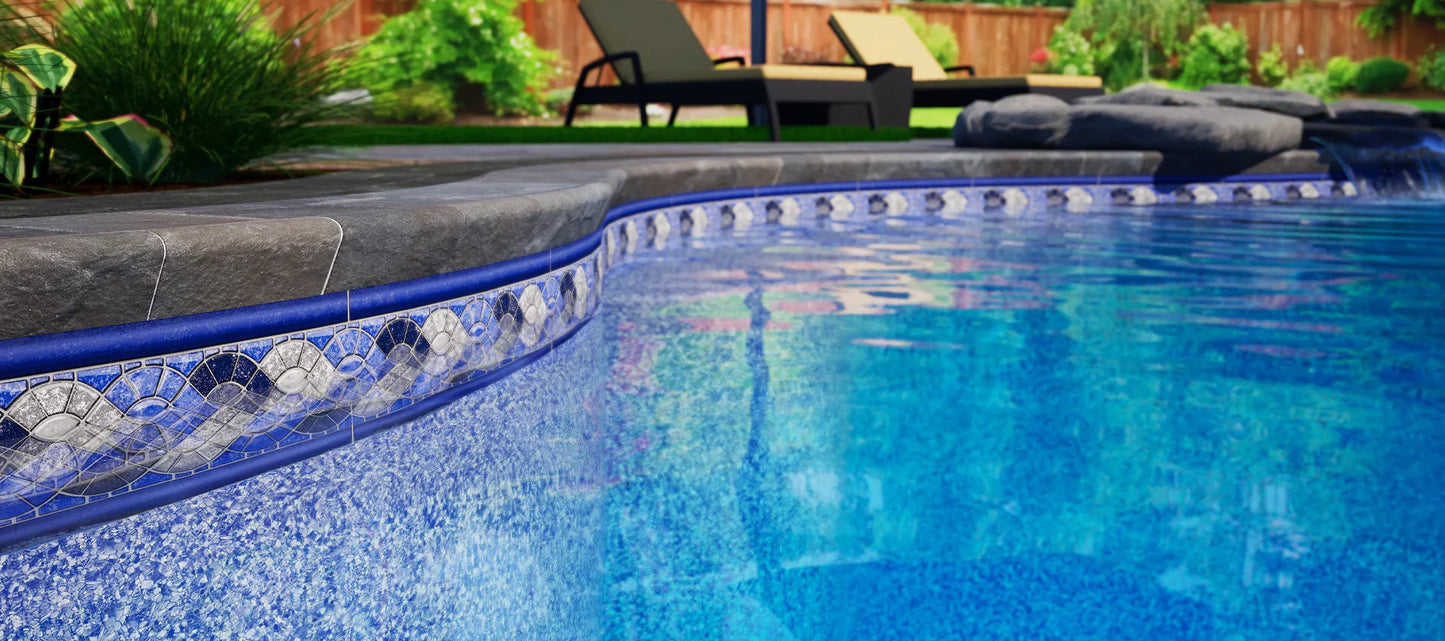 Rebord de piscine creusée avec margelle en pierre, eau bleue et décor de jardin