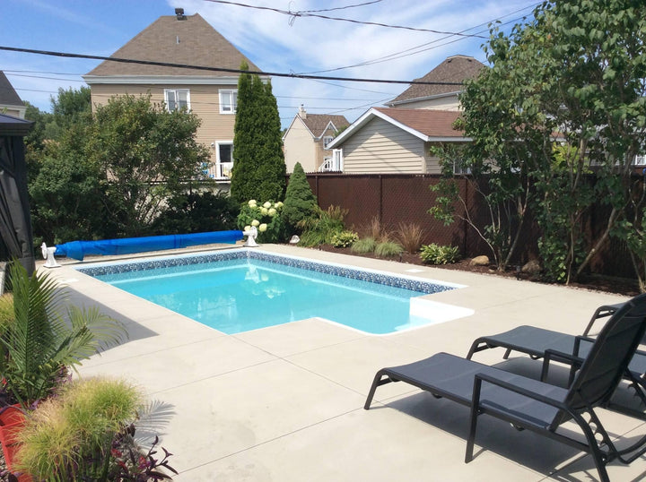 Piscine creusée moderne avec margelles en béton, terrasse et chaises longues dans un jardin paysager