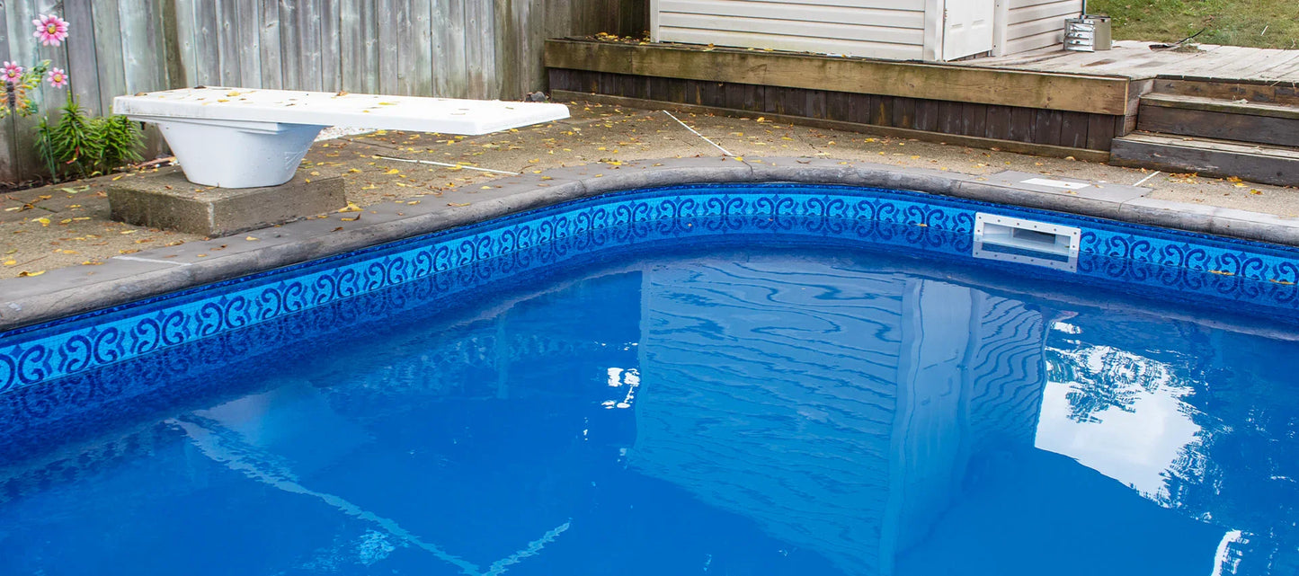 Piscine extérieure avec margelles grises et liner bleu motif géométrique, plongeoir blanc