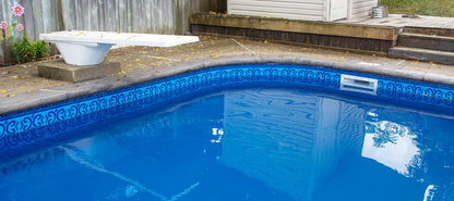 Piscine extérieure avec margelles grises et liner bleu motif géométrique, plongeoir blanc