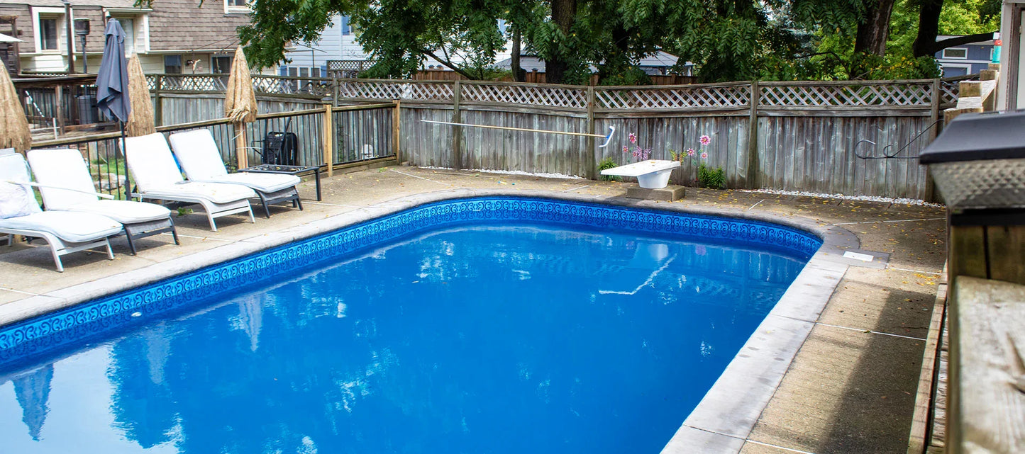 Piscine creusée avec eau bleue, margelle en béton, chaises longues et clôture boisée