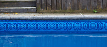 Bord de piscine bleu avec liner à motif géométrique, margelle en béton et clôture en bois