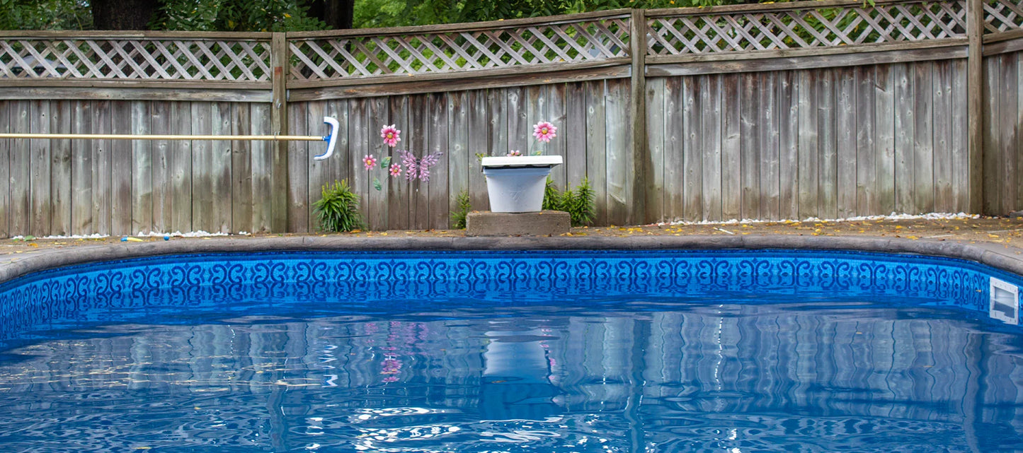 Piscine extérieure bleue avec motif, bord en béton, clôture bois et décoration florale