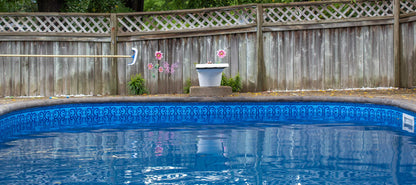 Piscine extérieure bleue avec motif, bord en béton, clôture bois et décoration florale