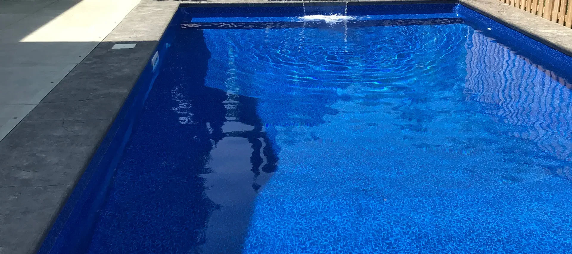 Piscine creusée rectangulaire moderne avec margelle grise et eau bleue scintillante