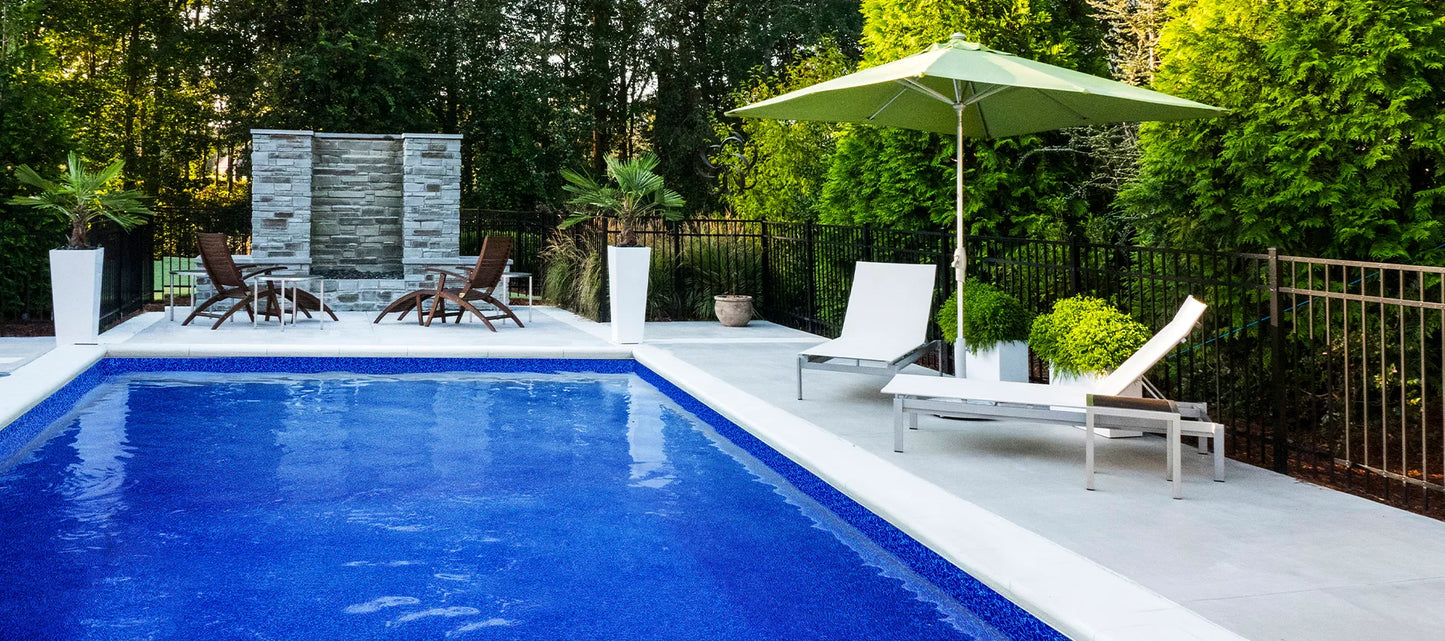 Piscine creusée moderne avec terrasse, chaises longues et parasol, entourée de verdure