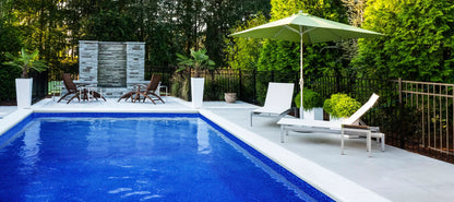 Piscine creusée moderne avec terrasse, chaises longues et parasol, entourée de verdure