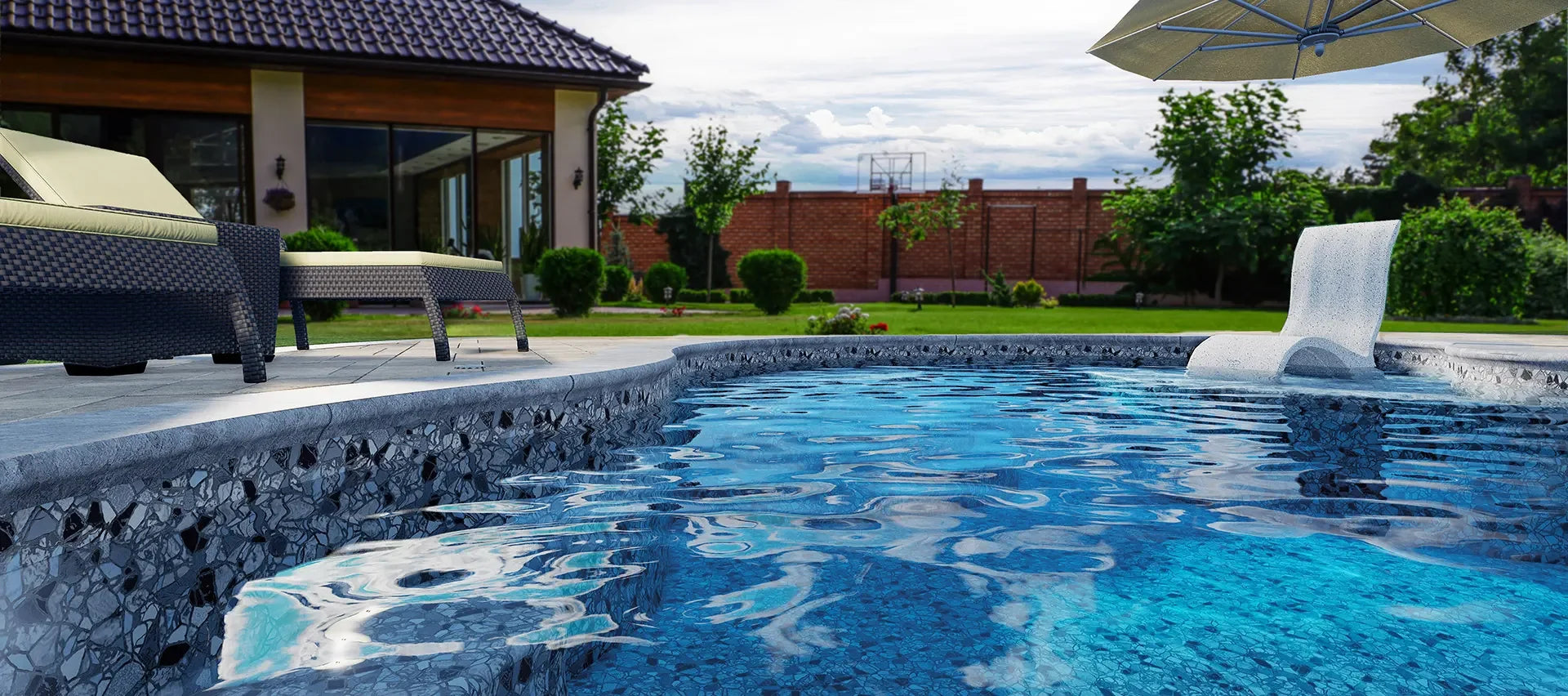 Piscine creusée extérieure moderne avec margelle en pierre, transat et jardin paysager