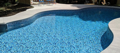 Piscine extérieure moderne avec finition en mosaïque bleue et terrasse en béton, ensoleillée.