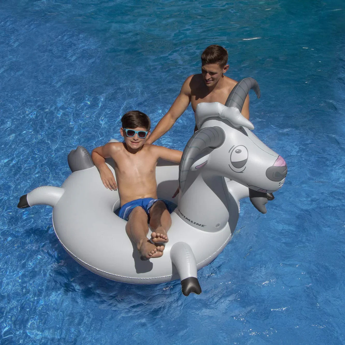 Garçon assis sur une bouée gonflable chèvre dans une piscine bleue en été