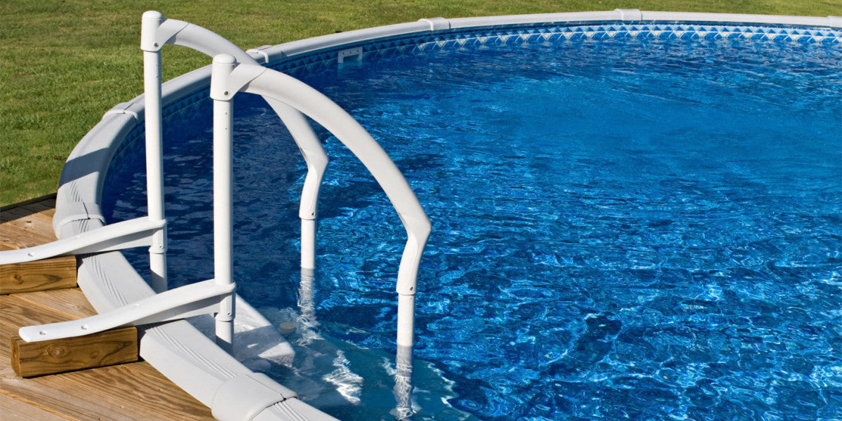 Piscine hors-sol avec marches d'accès blanches et eau claire, terrasse en bois autour.