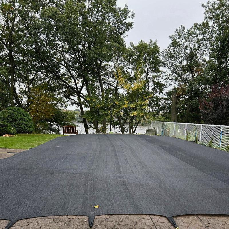 Couverture de piscine noire sécurisée sur piscine extérieure, jardin et arbres en arrière-plan