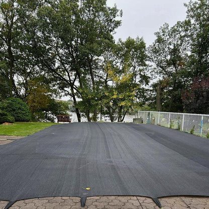 Couverture de piscine noire sécurisée sur piscine extérieure, jardin et arbres en arrière-plan