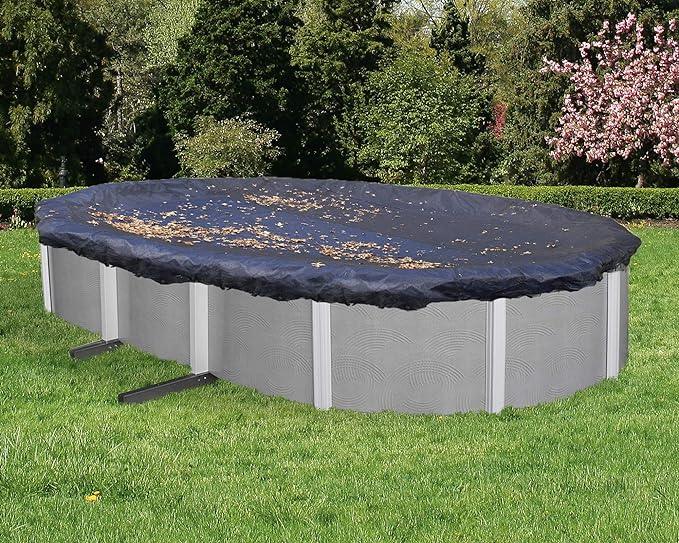 Piscine hors-sol ovale avec bâche de protection noire, feuilles sur la couverture, jardin verdoyant
