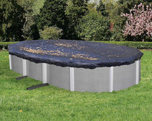 Piscine hors-sol ovale avec bâche de protection noire, feuilles sur la couverture, jardin verdoyant