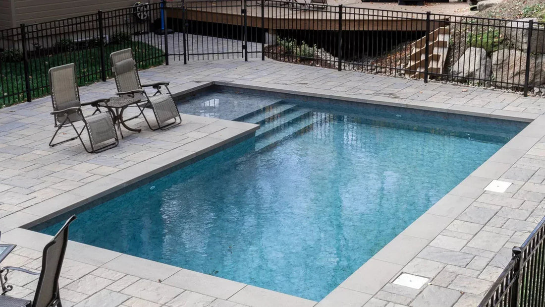 Piscine rectangulaire creusée moderne avec margelles en pierre et mobilier de jardin, sécurité clôturée.