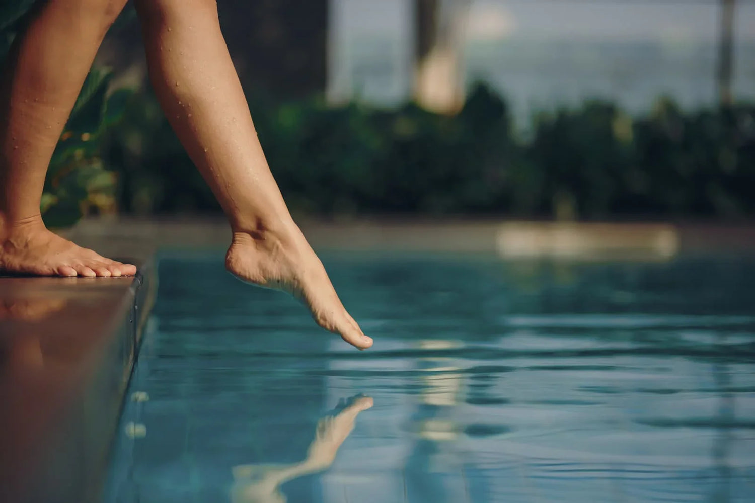 Personne touchant l'eau d'une piscine avec son pied, reflet sur l'eau claire extérieure