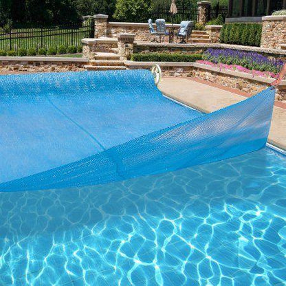 Couverture solaire bleue sur piscine extérieure, terrasse en pierre, jardin paysager