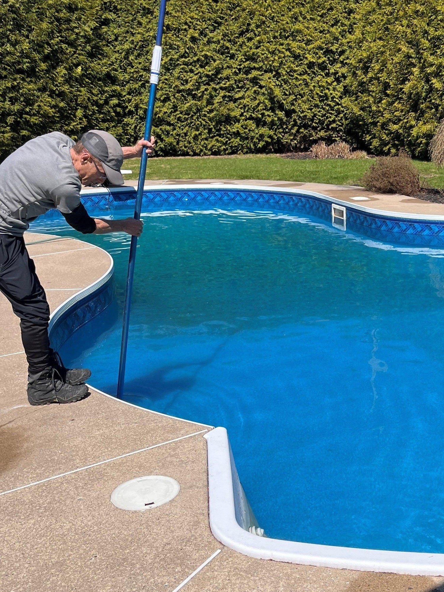 Technicien nettoyant une piscine extérieure avec perche, entretien piscine résidentielle